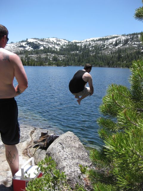 1971 Ford Bronco - A person leaps into a clear blue lake surrounded by pine trees and distant snow-covered mountains on a sunny day.