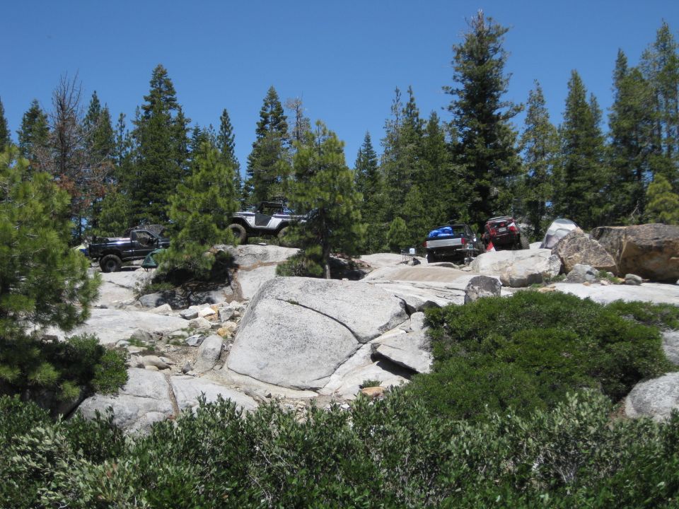 Several off-road vehicles navigating a rocky, wooded area under a clear blue sky