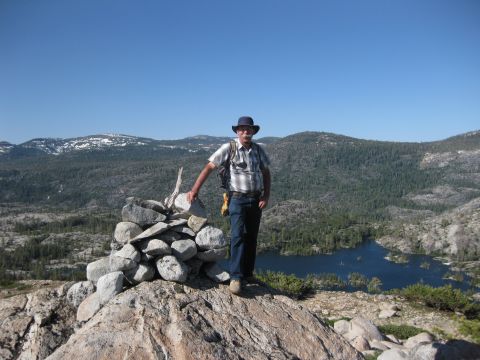 1971 Ford Bronco - A man poses for a photo on a rocky peak with a lake and forested mountains in the background.
