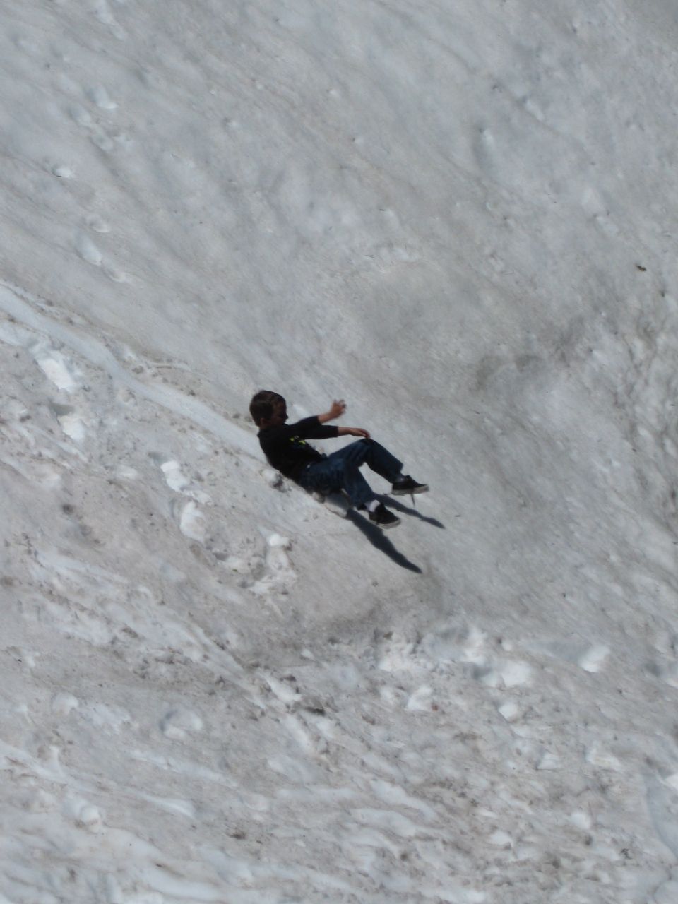 Kid sliding down a snowy hill, casting a shadow