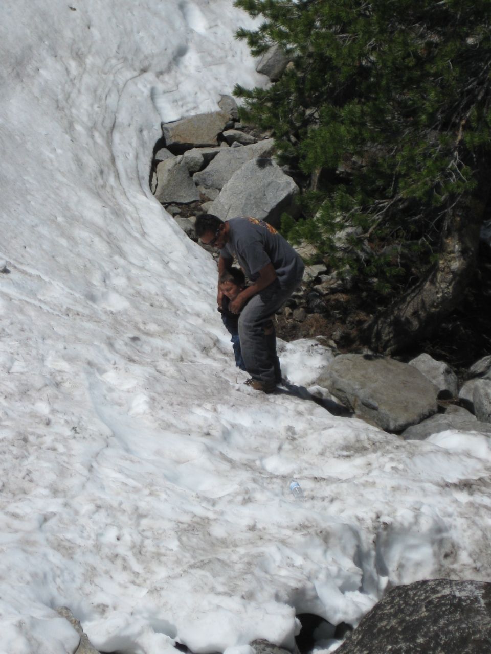 Two people on a snow-covered rocky mountainside with pine trees