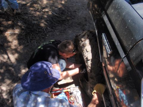 1971 Ford Bronco - Two individuals are seen attending to the tire of a black SUV in an outdoor setting.