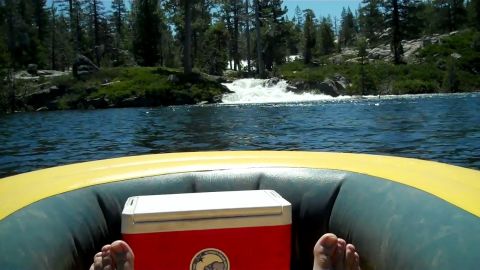 1971 Ford Bronco - View from inside an inflatable raft, showing a cooler and feet, with a river and waterfall ahead.