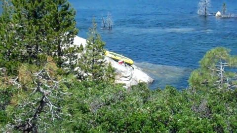 1971 Ford Bronco - A kayak sits on a rock formation next to a body of water, with trees in the foreground and background.