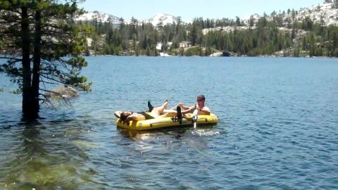 1971 Ford Bronco - Two people relax on an inflatable raft in a lake surrounded by trees and mountains.
