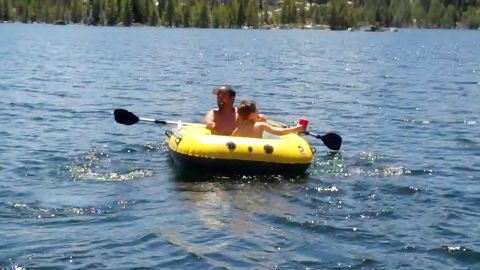 1971 Ford Bronco - Two people enjoy a day on the water in a yellow inflatable boat, paddling across a calm lake with trees in the background.
