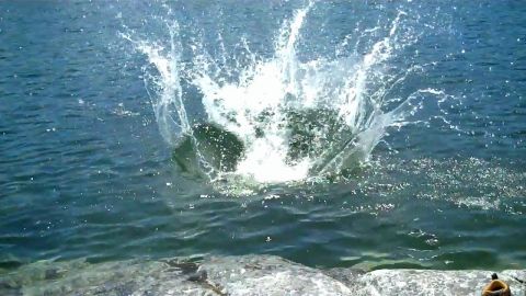 1971 Ford Bronco - A large splash erupts from the water, with rocks visible in the foreground and a website logo at the bottom right.