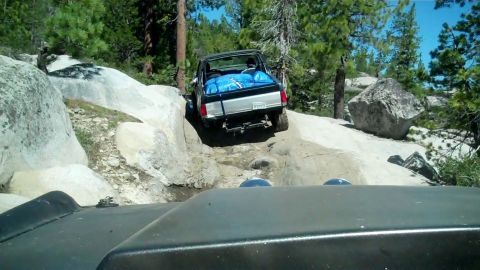 1971 Ford Bronco - A black pickup truck navigates a rocky trail, loaded with blue cargo.