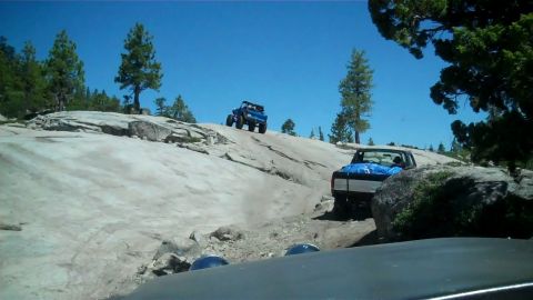 1971 Ford Bronco - Two off-road vehicles navigate a steep, rocky incline under a clear blue sky, with one vehicle in the foreground and another further up the…