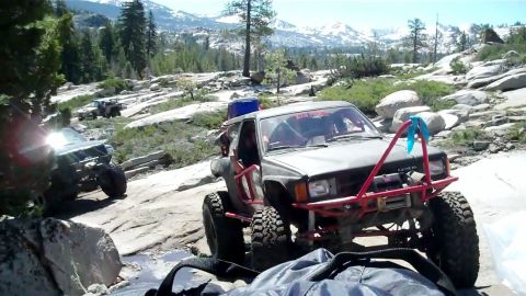 1971 Ford Bronco - Multiple modified off-road vehicles traverse a challenging rocky path in a mountainous landscape.