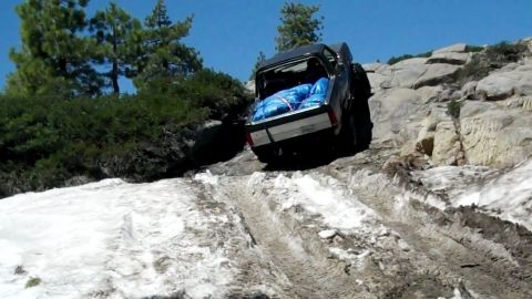 1971 Ford Bronco - A black off-road vehicle navigates a challenging rocky and snowy terrain.