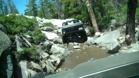 1971 Ford Bronco - A black pickup truck navigates a challenging rocky stream in a wooded area.