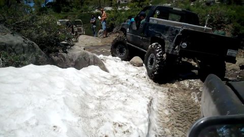 1971 Ford Bronco - A black pickup truck maneuvers through a challenging off-road course with snow and rocky terrain.