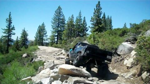 1971 Ford Bronco - Off-road truck tackling a challenging rocky path in a mountainous, wooded area.