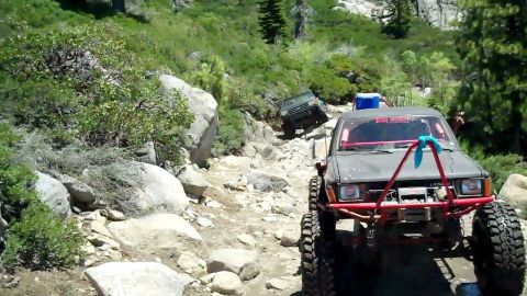 1971 Ford Bronco - Two off-road vehicles navigate a challenging, rocky mountain trail under a clear sky.