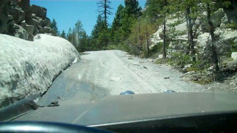 1971 Ford Bronco - Driving on a rough dirt road with snow on the side, surrounded by trees and rocks.