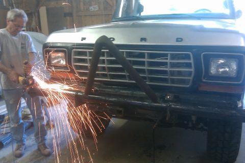 1978 Ford Bronco - A man uses an angle grinder on the front bumper of a Ford truck in a garage setting, creating a shower of sparks.