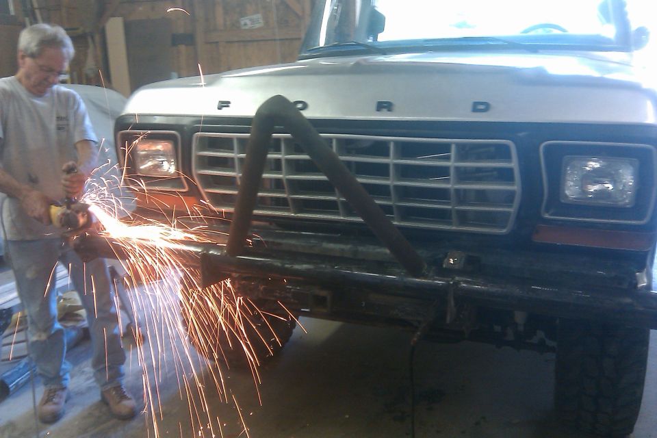 Man grinding on front bumper of a Ford truck. Grille has horizontal bars and a triangular brush guard