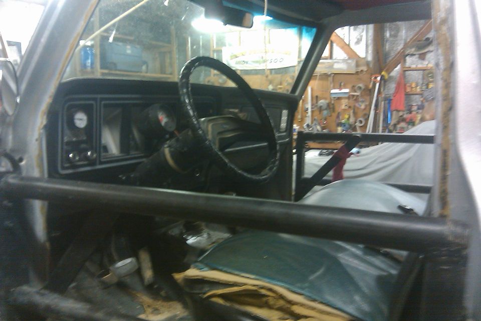 Interior shot of a vehicle with a roll cage, dashboard, and steering wheel visible. The vehicle appears to be in a workshop