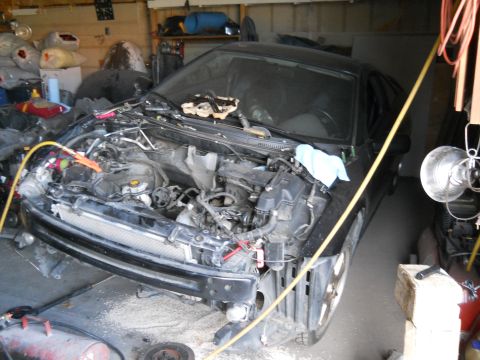 2006 Ford E350 - A black car is in a garage with its front end disassembled, showing the engine and various parts.