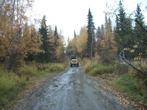 1979 Ford Bronco - Two SUVs navigate a muddy dirt road surrounded by trees in fall colors.