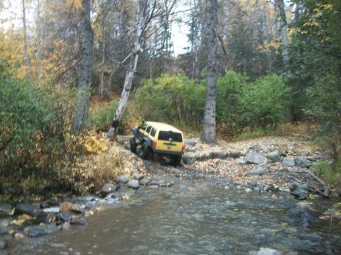1979 Ford Bronco - A yellow SUV is shown off-roading through a stream in a forest setting.