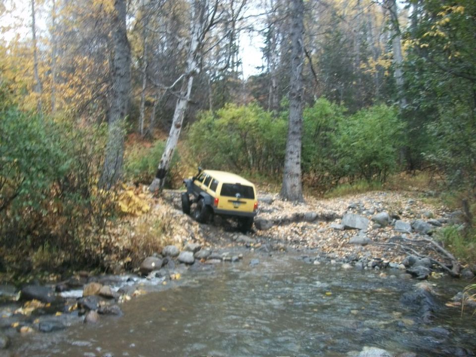Yellow SUV navigating a rocky stream bed in a wooded area during autumn