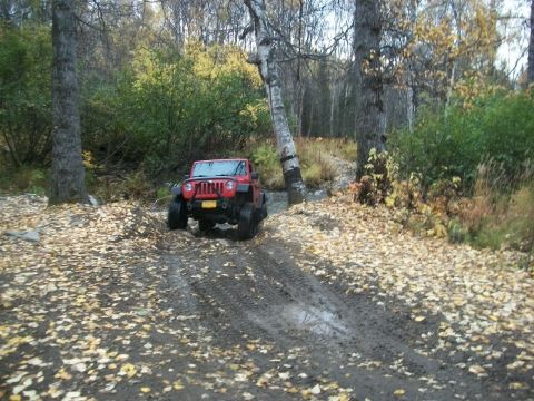 1979 Ford Bronco - A red Jeep Wrangler navigates a challenging off-road path through autumn foliage.