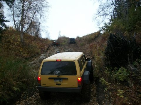1979 Ford Bronco - A yellow Jeep Cherokee XJ navigates a challenging rocky trail with other vehicles in the background.