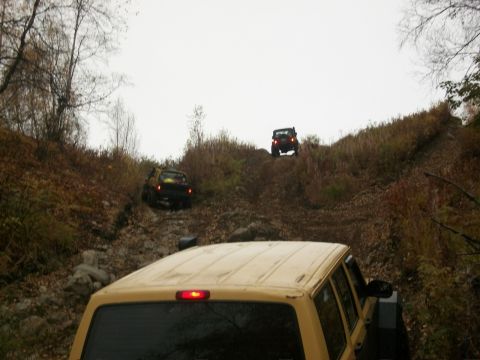 1979 Ford Bronco - Multiple off-road vehicles navigate a challenging, wooded incline during an autumn excursion.