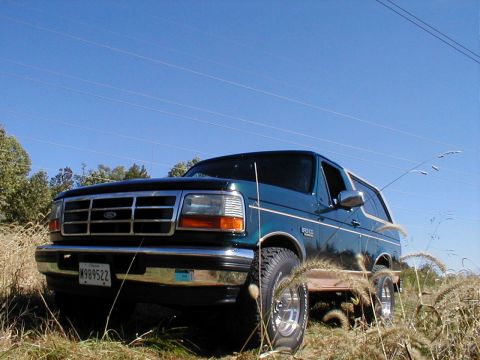 1995 Ford Bronco - Teal 1995 Ford Bronco parked in a grassy field under a clear blue sky.
