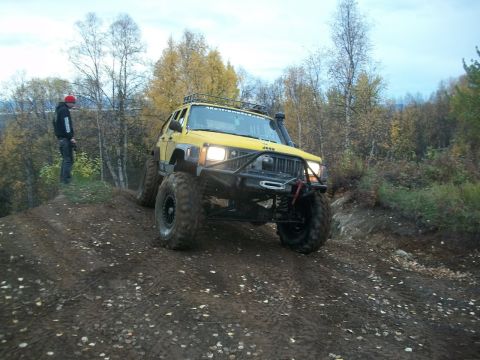 1979 Ford Bronco - Modified yellow Jeep Cherokee navigates a steep dirt incline during an off-road excursion.
