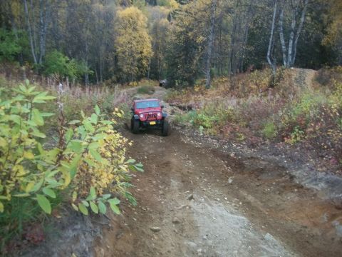 1979 Ford Bronco - A red Jeep navigates an off-road trail surrounded by autumn foliage.