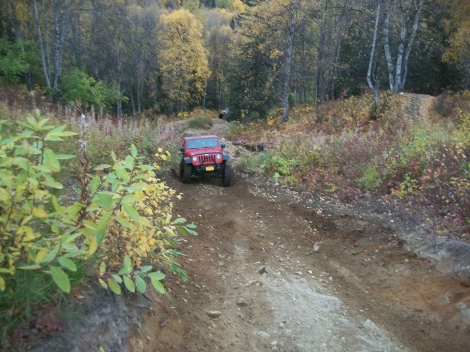 Red Jeep Wrangler driving up a dirt trail in a wooded area with fall colors
