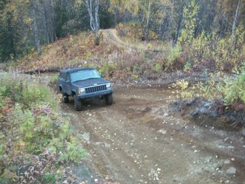 1979 Ford Bronco - A dark gray Jeep Cherokee XJ navigates a dirt path through an autumn forest.