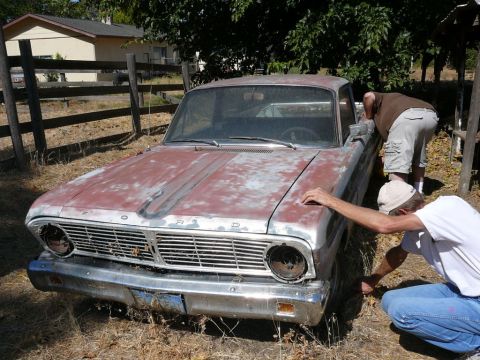 1988 Ford Bronco - Two men inspect the front of a weathered 1963 Ford Falcon parked outdoors.