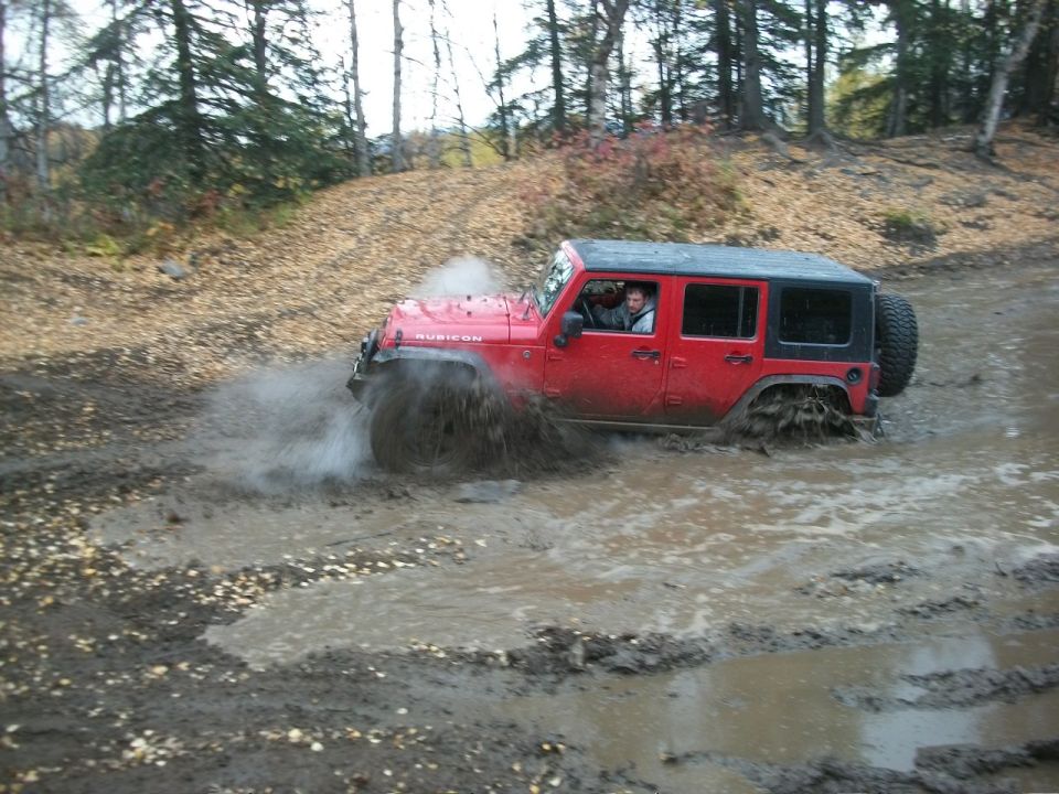 Red Jeep Wrangler Rubicon driving through mud puddle