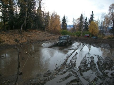 1979 Ford Bronco - Multiple off-road vehicles are seen struggling through a muddy terrain with trees in the background.