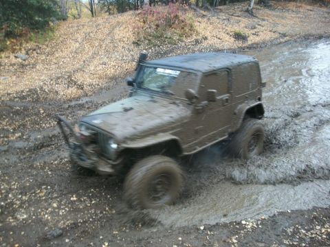 1979 Ford Bronco - This off-road vehicle is navigating a challenging muddy terrain, kicking up water and mud as it goes.