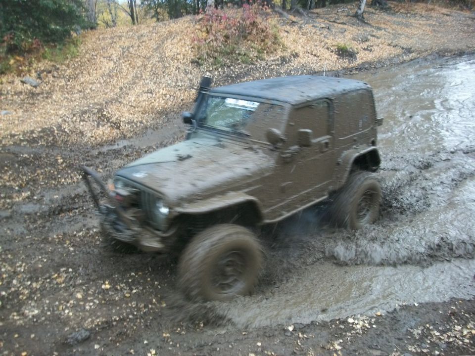 Muddy off-road vehicle driving through a muddy track with trees in the background