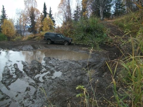 1979 Ford Bronco - An off-road vehicle navigates a challenging muddy path with a large water obstacle.