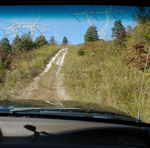 1995 Ford Bronco - View from inside a vehicle driving on a dirt road towards power line towers.