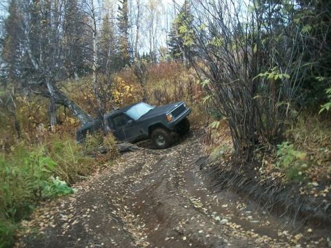 1979 Ford Bronco - A dark SUV navigates a challenging off-road trail surrounded by autumn foliage.