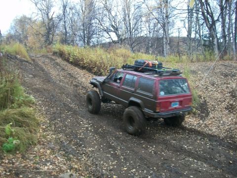 1979 Ford Bronco - Modified Jeep Cherokee XJ navigates a muddy, leaf-covered trail during an off-road excursion.
