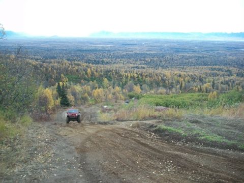 1979 Ford Bronco - A red SUV navigates a dirt path through a forest with fall foliage.