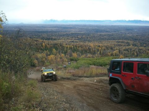 1979 Ford Bronco - Multiple off-road vehicles navigate a dusty trail through a wooded landscape.