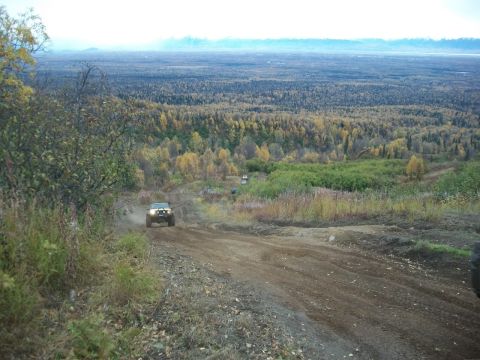 1979 Ford Bronco - Several vehicles navigate a dirt path through a wooded, hilly landscape during autumn.