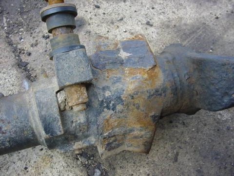 1992 Ford Bronco - Extreme close-up of a rusty steering knuckle arm with a tie rod end clamped into its tapered bore by a pinch bolt and castle nut, resting o…