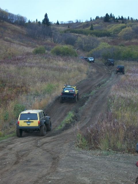 1979 Ford Bronco - A convoy of off-road vehicles navigates a challenging dirt path through a grassy, wooded landscape.