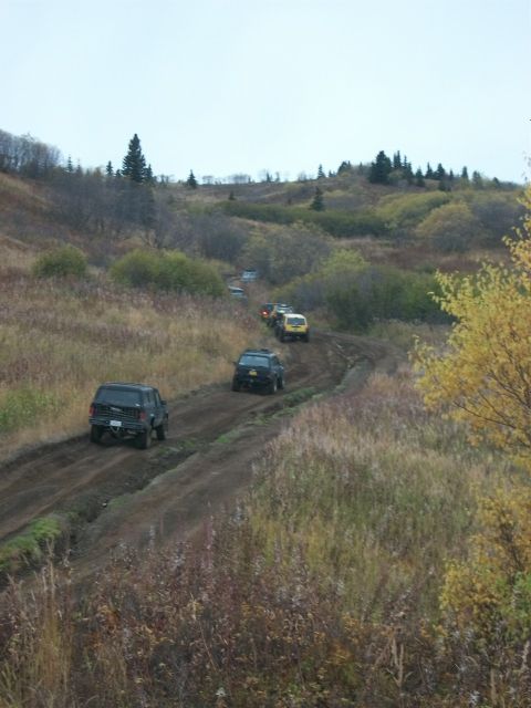 1979 Ford Bronco - A line of SUVs navigates a dirt path through a rural, autumnal landscape.